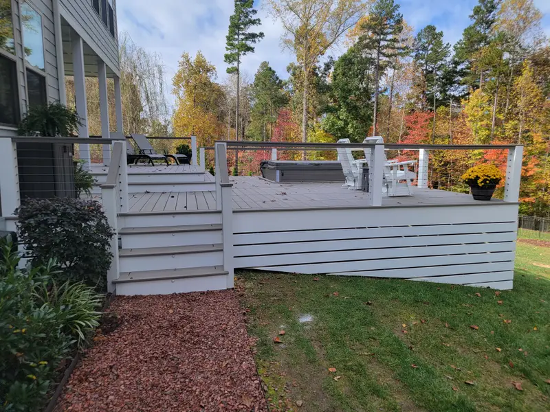 Deckorators composite deck with cable railing, white posts, and hot tub backing to fall woods