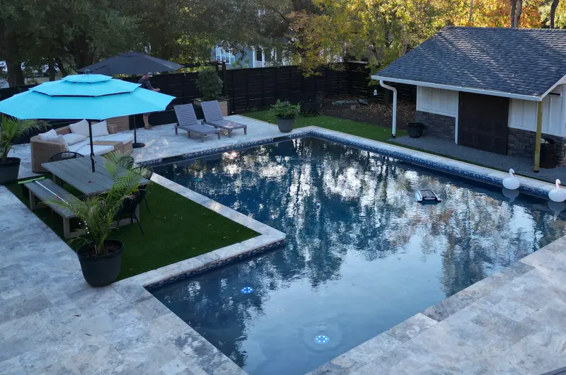 Custom pool with travertine paver deck, turf insets, lounge seating, and pool house