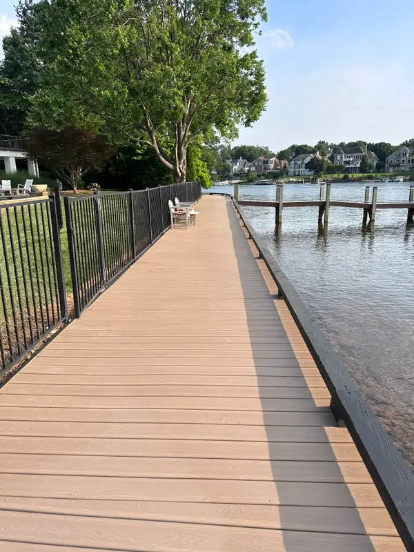 Long composite walkway deck running the length of a lake seawall, black aluminum fence on one side and a dock on the other