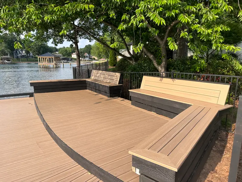Waterfront deck with built-in composite bench seating wrapping two sides, shaded by a mature hardwood