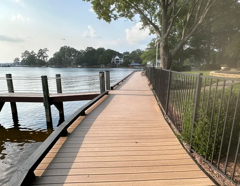 Composite waterfront walkway curving along the shoreline past a wood pier at dusk