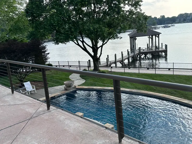 Cable-railed pool terrace overlooking the lake, with a covered boat dock and pier beyond
