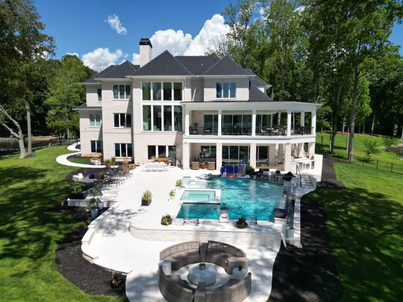 Aerial of the same home showing the curved pool deck, spa, and a circular fire-pit seating area set into the lawn