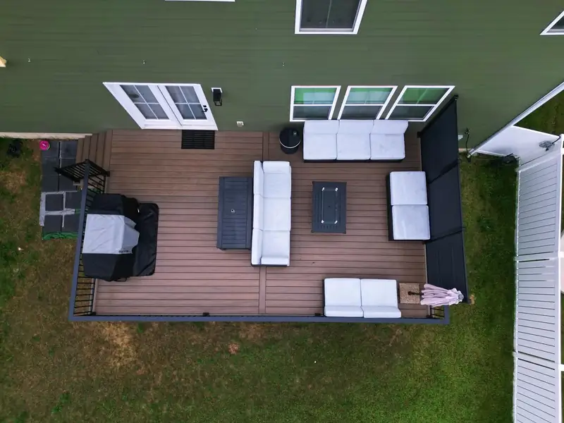 Overhead view of a composite deck with an outdoor sectional, coffee table, and grill against a green-roofed house