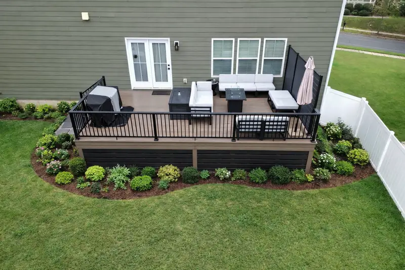 Elevated composite deck with black aluminum railing and French doors, edged by a newly planted shrub bed