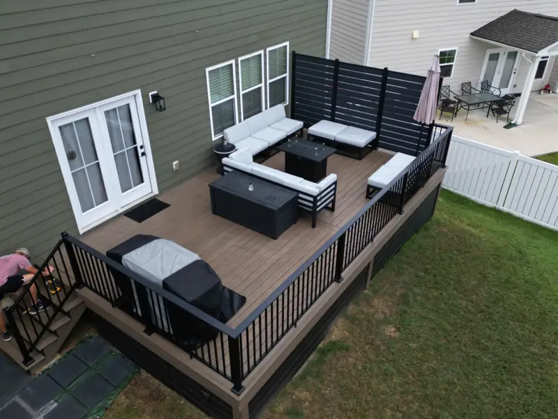 Composite deck with a black horizontal privacy screen, L-shaped outdoor sectional, and storage bench