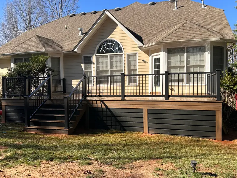 Rear of a tan single-story home with a new composite deck, black aluminum railing, and dark board skirting