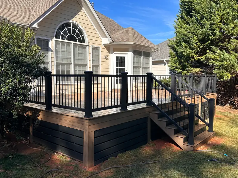 Corner view of the composite deck showing black railing, matching stair rail, and dark horizontal skirting