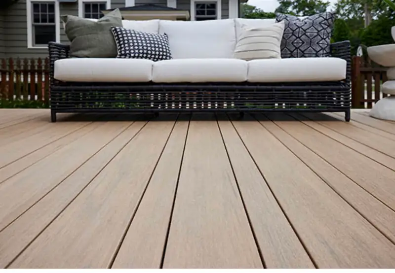 Close-up of warm-toned composite deck boards with a wicker sofa and cushions behind