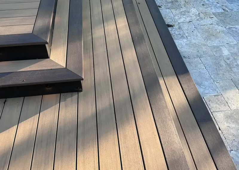 Detail of composite decking meeting a travertine patio, with dark-stained stair treads and riser lighting