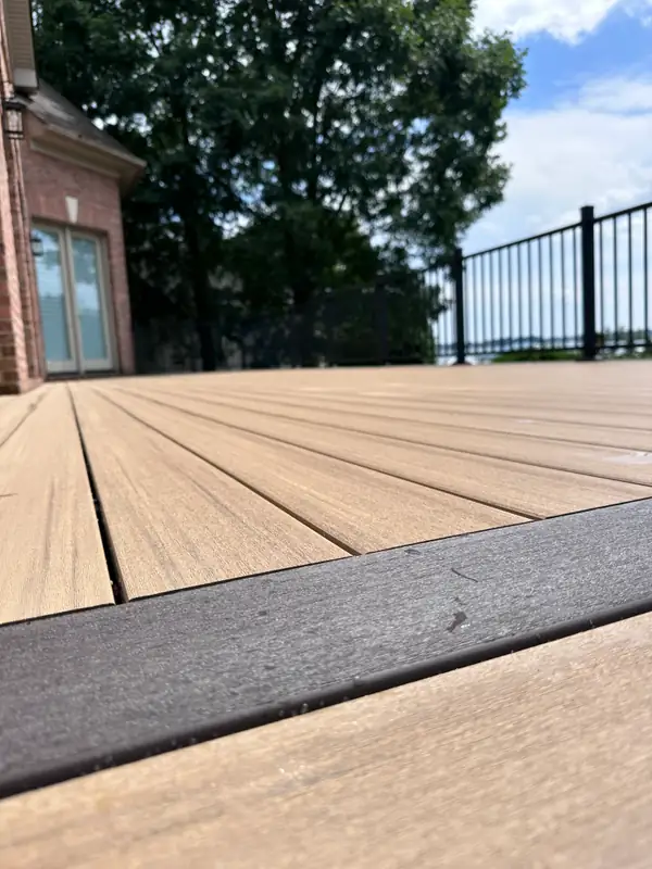 Low-angle detail of composite deck boards with a contrasting dark border board and black railing