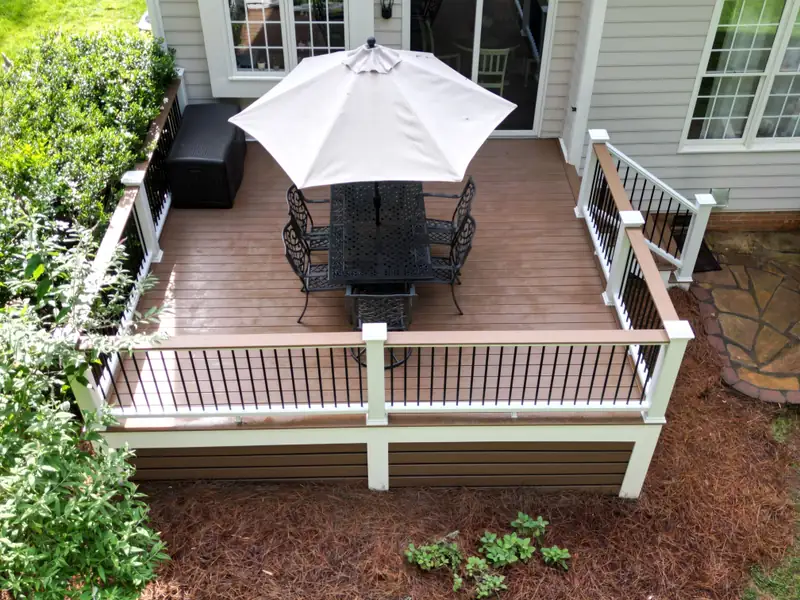 Small backyard deck with white railing posts, black balusters, a patio table, and an open umbrella