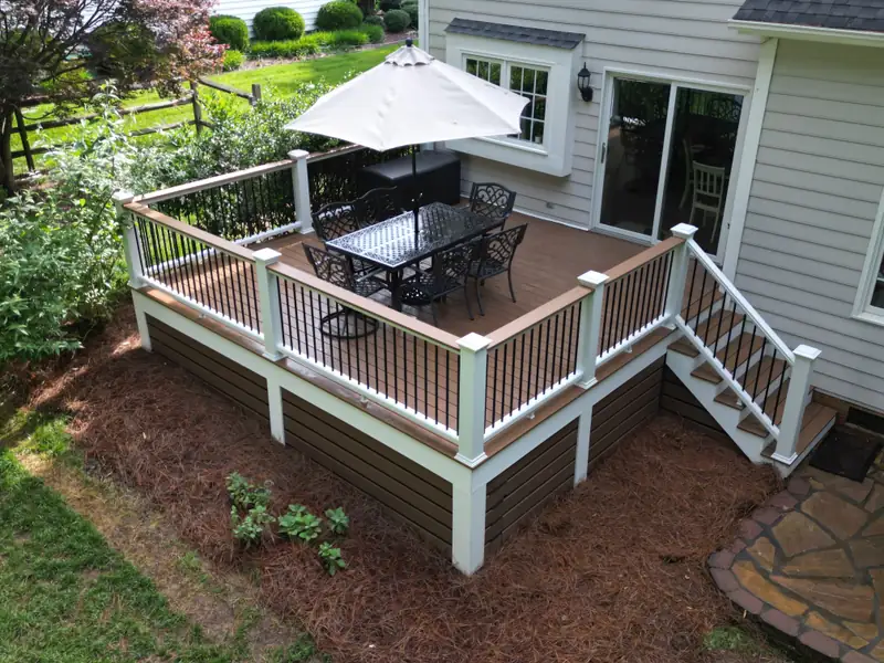 Overhead view of the square deck showing white posts, black balusters, dining set, and stairs down to the lawn