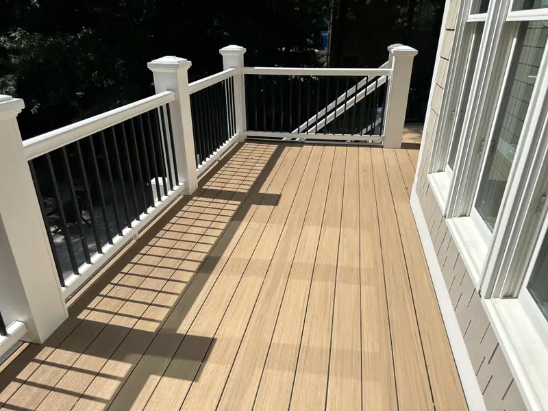 Composite deck landing with white railing posts, black balusters, and a stair down to the yard