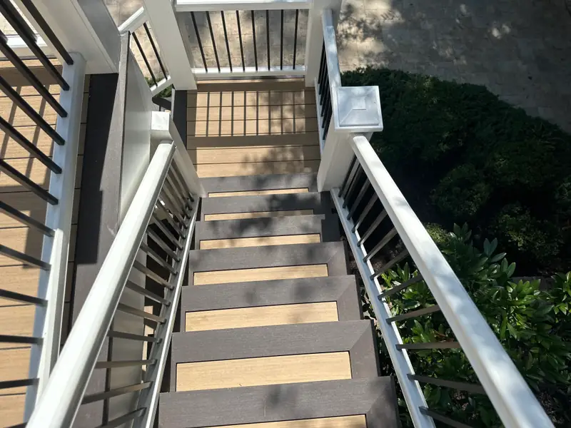 Looking down a composite stair with alternating light and dark treads, white posts, and black balusters