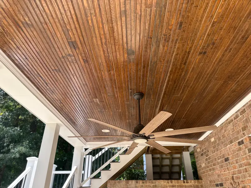 Stained tongue-and-groove porch ceiling with a large black ceiling fan and recessed lighting