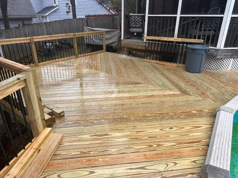 Freshly built pressure-treated wood deck, boards still wet, laid in a diagonal pattern with wood railing