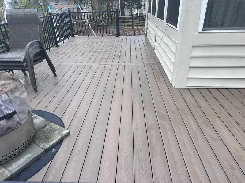 Warm brown composite deck with black aluminum railing, patio chairs, and a fire bowl on a stone base
