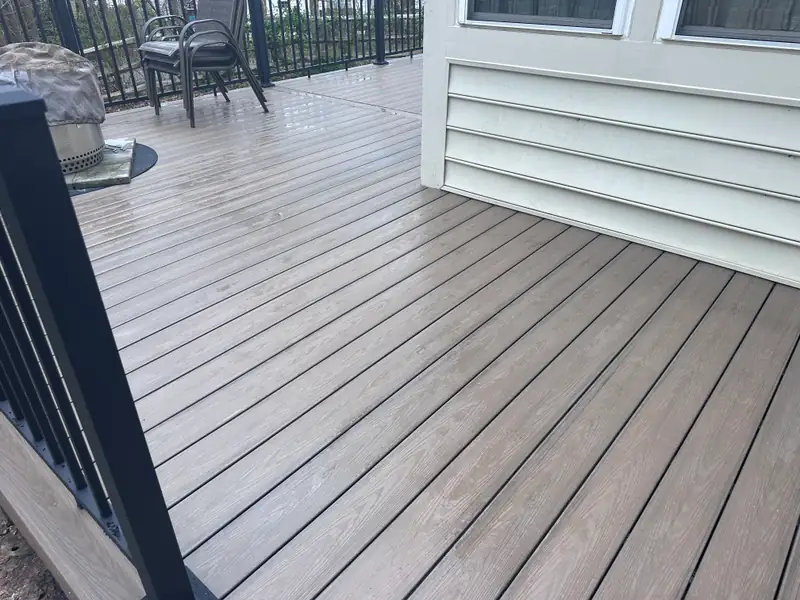 Weathered-gray composite deck boards running up to the house wall, with black railing and a dining set