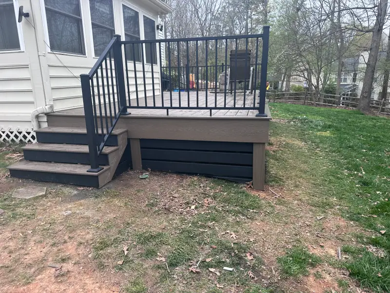 Compact composite deck with black aluminum railing, dark skirting, and steps down to the yard