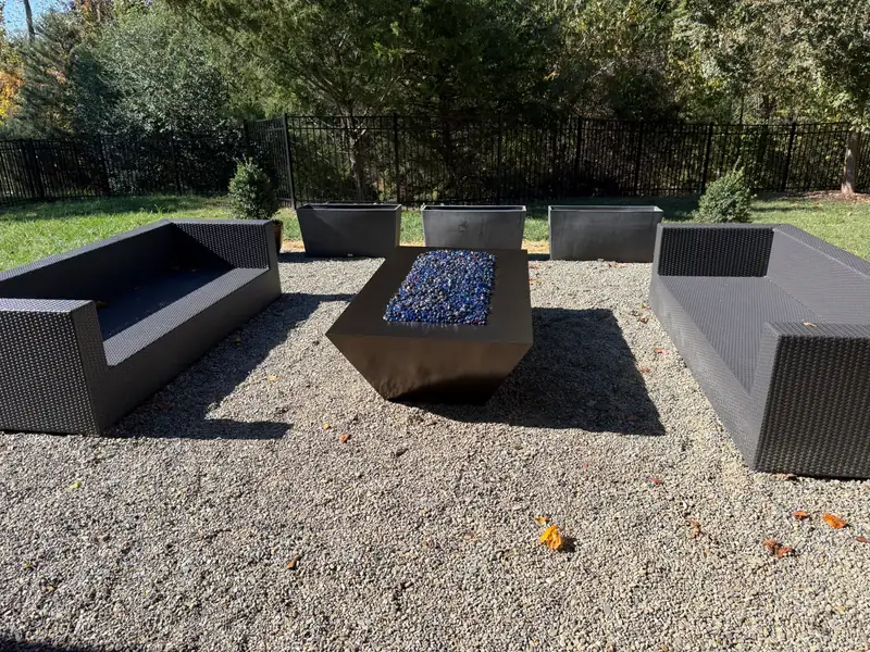 Gravel fire-pit lounge with modular outdoor sofas and planters set around a linear gas fire table