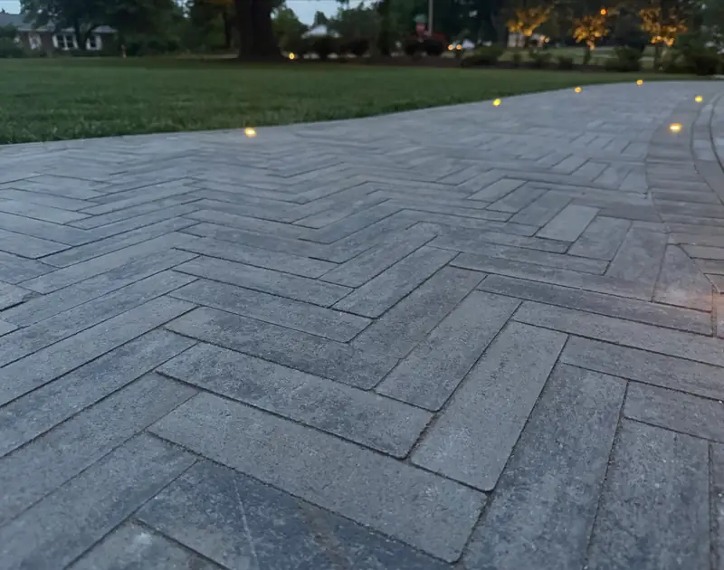 Close view of the herringbone paver field and border course, path lighting glowing at dusk