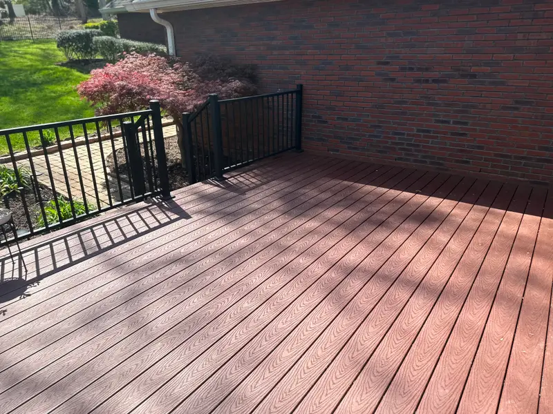 Capped composite deck boards in a warm woodgrain finish with black aluminum railing against a brick wall