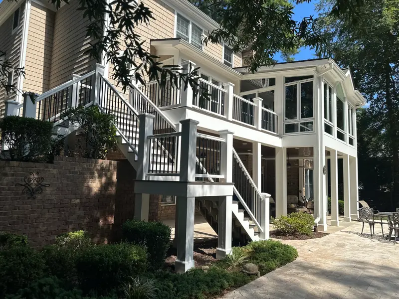 Elevated white deck with black aluminum balusters and stairs alongside a screened porch on a brick home