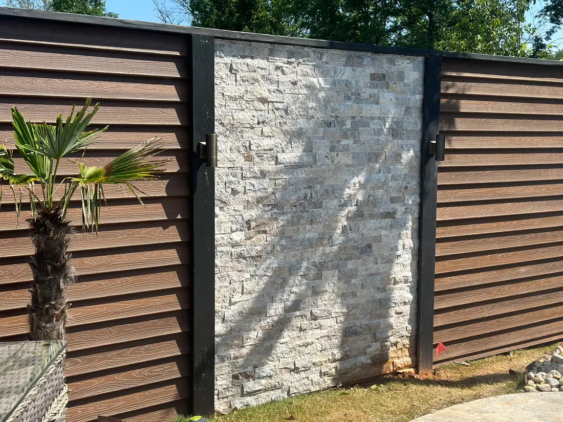 Stacked-stone feature wall flanked by horizontal composite slat privacy screens with black posts and wall-mounted lighting